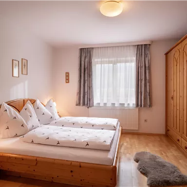 Ein gemütliches Schlafzimmer mit zwei Einzelbetten und holzigen Möbeln. Das Zimmer ist hell und freundlich, mit einem Fenster, das viel Licht hereinlässt.