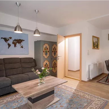 Ein modernes Wohnzimmer mit einem bequemen Sofa, einem Tisch und einer Essgruppe. An der Wand hängt eine Weltkarte und der Raum ist hell und einladend.