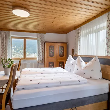 Ein gemütliches Schlafzimmer mit einem großen Bett und Holzdetails. Große Fenster sorgen für viel Tageslicht und eine angenehme Atmosphäre.