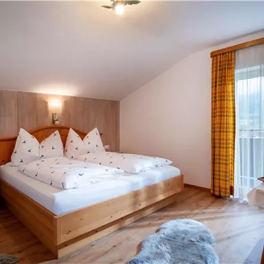 Ein gemütliches Schlafzimmer mit einem Doppelbett und traditionellen Kissen. Große Fenster sorgen für viel Licht und bieten einen schönen Ausblick.