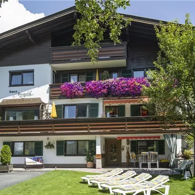Ein charmantes Gasthaus mit üppigen Blumen und einem gepflegten Garten. Liegen stehen bereit, um die sonnige Umgebung zu genießen.