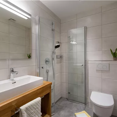 Ein modernes Badezimmer mit einer Dusche aus Glas und einem eleganten Waschbecken. Es enthält auch eine helle Wandgestaltung und kleine Pflanzen als Dekoration.