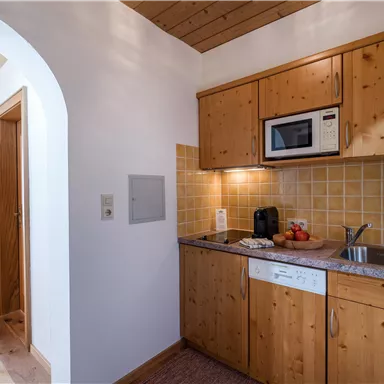 Eine gemütliche Küche mit Holzmöbeln und modernen Geräten. Die Wände sind hell, und es gibt eine kleine Arbeitsfläche mit einer Spüle und einem Mikrowellenofen.