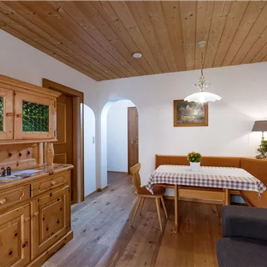 Ein gemütlicher Essbereich mit Holzmöbeln und einem Tisch mit kariertem Tischdecken. Die Wände sind hell und die Decke aus Holz verleiht dem Raum eine warme Atmosphäre.