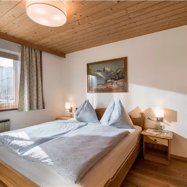 Ein gemütliches Schlafzimmer mit einem Doppelbett und Holzverkleidung. Es gibt ein Fenster mit Vorhängen und ein Bild an der Wand.