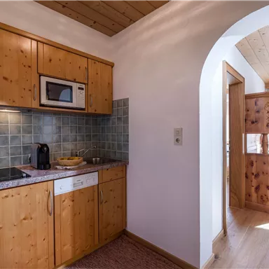 Eine moderne Küchenecke mit Holzmöbeln und einer hellen, freundlichen Atmosphäre. Es gibt einen Herd, eine Mikrowelle und eine Spüle in der Küche.