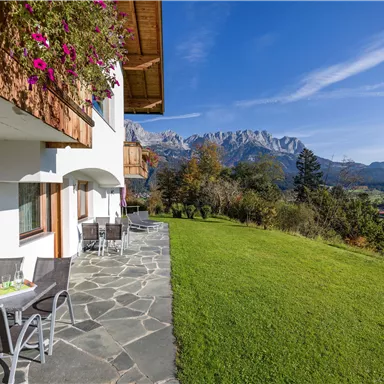 Eine schöne Aussicht auf die Berge von einem Garten mit Rasen. Auf der Terrasse stehen Tische und Stühle, um die Natur zu genießen.