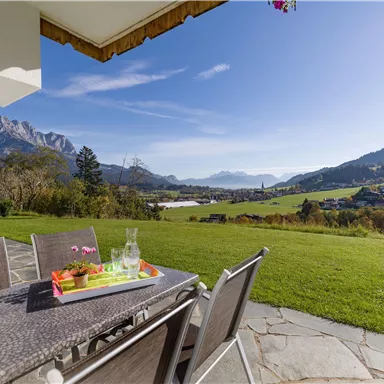 Eine Terrasse mit modernem Möbeln bietet einen Blick auf die Hügel und Berge. Der Himmel ist klar und die Umgebung ist grün und einladend.