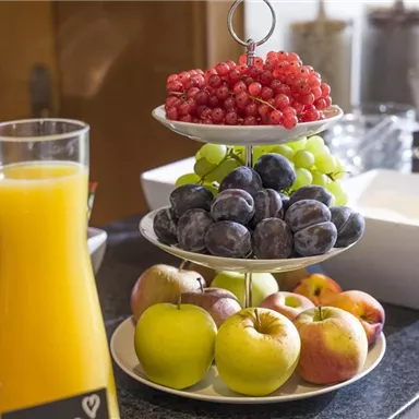 A decorative fruit plate with red currants, grapes, plums, and apples. Next to it are glasses of freshly squeezed orange juice.