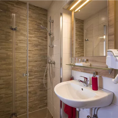 A modern bathroom with a shower and sink. The walls are brightly tiled and there are large mirrors.