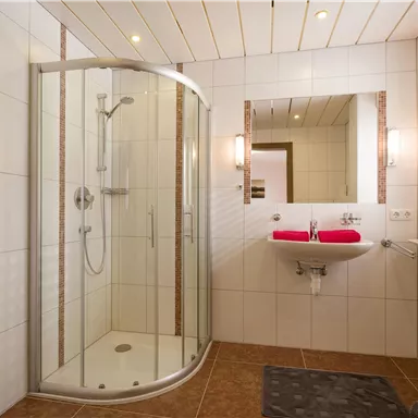 A modern bathroom with a round shower cubicle and bright tiles. The room is well-lit and has a simple, elegant furnishings.