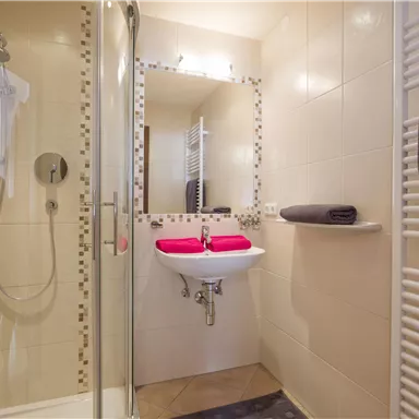 A modern bathroom with a shower and a sink. The walls are brightly tiled and towels are ready.