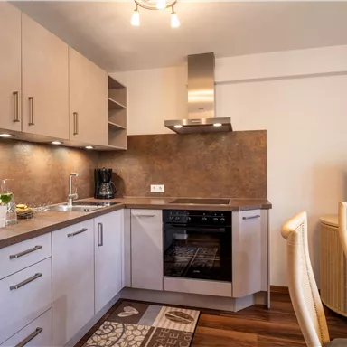 A modern kitchen with bright furniture and stainless steel appliances. The floor is made of wood and there is a dining area with a table and chairs.