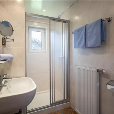 A modern bathroom with a shower, a sink, and a towel rack. The walls are brightly tiled, and there are two towels in soft colors.