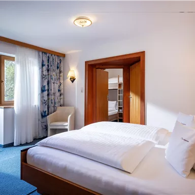 A cozy room with a large bed and a bright, friendly atmosphere. There is a balcony with a view outside and a quiet seating area.