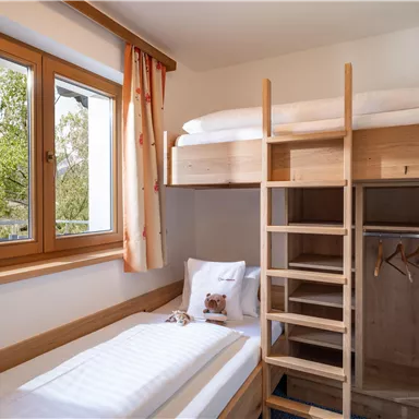 A bright room with a loft bed and a single bed. Large windows let in plenty of daylight and offer a view of nature.