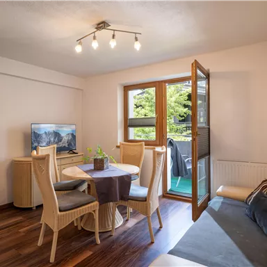 A cozy living kitchen with a dining table and chairs. Through the window, there is a view of the outdoor area.
