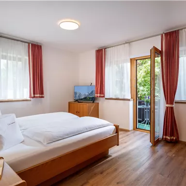 A bright bedroom with a double bed and large windows. A balcony and a television are also present in the room.