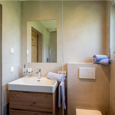 A modern bathroom with a bright sink and wooden accents. There is a window that allows natural light to come in.