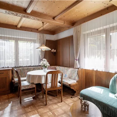 A cozy dining area with wooden furniture and a round table. Large windows let in a lot of light and create an inviting atmosphere.