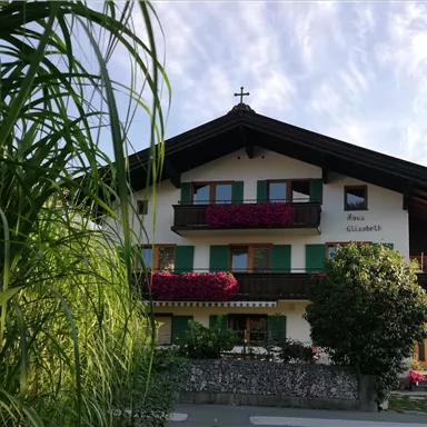 A traditional house with a wooden roof and colorful flowers on the balconies. The surrounding vegetation gives the image an inviting atmosphere.