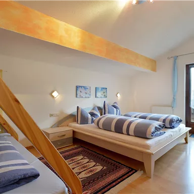 Ein helles Schlafzimmer mit zwei Betten, die mit gestreiften Bettwäsche dekoriert sind. Große Fenster sorgen für viel Tageslicht und eine angenehme Atmosphäre.