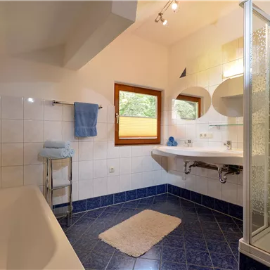 Ein helles Badezimmer mit einer Badewanne und einer Dusche. Die Wände sind gefliest, und es gibt ein Fenster, das natürliches Licht hereinlässt.