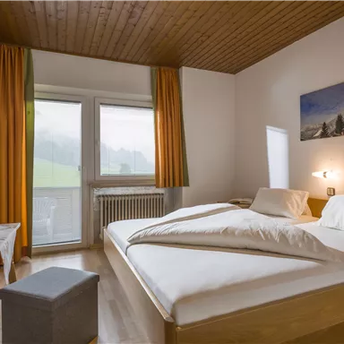 A modern bedroom with a double bed and a cozy wooden ceiling. Large windows let in plenty of light and offer a view of the greenery.