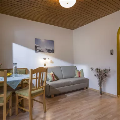 A cozy living space with a table and chairs as well as a sofa. A warm atmosphere with wooden ceilings and a small window that lets in light.
