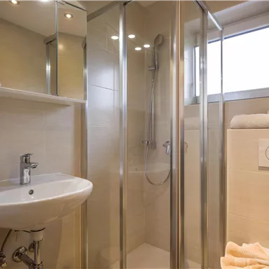 A modern bathroom with a shower cabin and a sink. Bright tiles and a window create a friendly atmosphere.