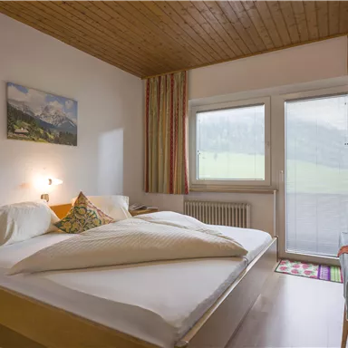 A cozy bedroom with a double bed and bright walls. Large windows provide a view of the surrounding landscape.