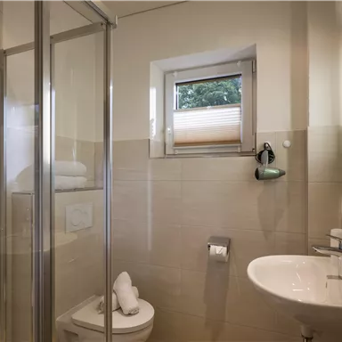 A modern bathroom with a shower and a sink. Bright walls and a window create a friendly atmosphere.