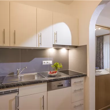 A modern kitchen with bright cabinets and a countertop. In the background, a cozy bedroom is visible.