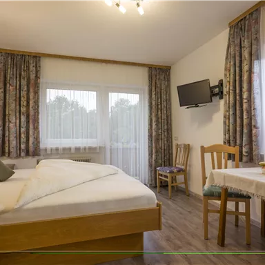 A cozy bedroom with a double bed and a table. Bright curtains and a pleasant atmosphere make the room inviting.