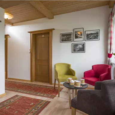 An inviting hallway with colorful armchairs and a small table. Pictures hang on the wall, and a rug adds coziness to the space.