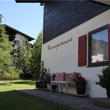 A cozy vacation apartment with blooming plants in front of the door. The garden is green and inviting, perfect for relaxation.
