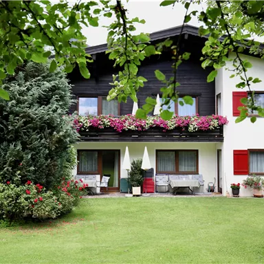 An inviting house with blooming plants and red shutters. The garden is green and well-maintained, ideal for outdoor relaxation.