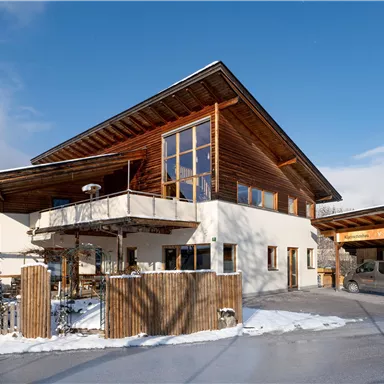 A modern house with wooden cladding and large windows. Outside, there is snow and the sky is blue.