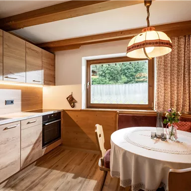 A modern kitchen with wooden furniture and a round table. Natural light comes through the window and there is a cozy atmosphere.