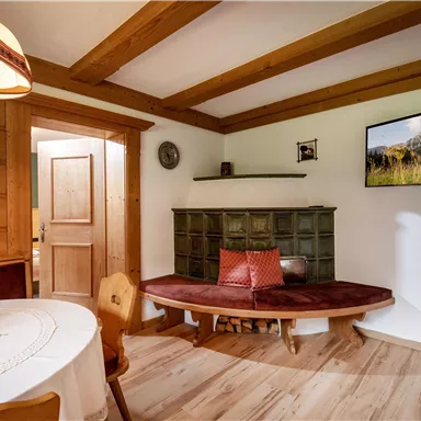 A cozy room with wooden paneling and a round table. A picture of a mountain landscape hangs on the wall, and a bench invites relaxation.
