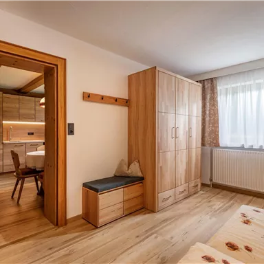 A cozy room with wooden cabinets and a large window. The floor is made of wood, and in the background, you can see a dining area.