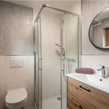 A modern bathroom with a shower and a sink. Towels and a window overlooking the outdoors complete the space.