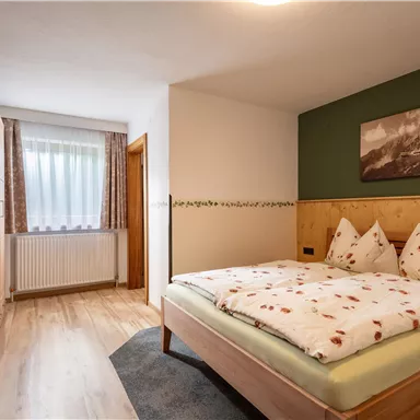 A cozy bedroom with a large bed and cool wooden furniture. The room has large windows and a decorative picture on the wall.