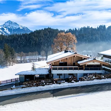 Ein schönes Winterhaus umgeben von schneebedeckten Feldern und Bergen. Der Himmel ist klar und der Schnee glitzert in der Sonne.