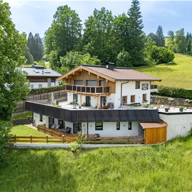 A modern house in a green landscape with trees and meadows. The architecture features balconies and a cozy terrace.