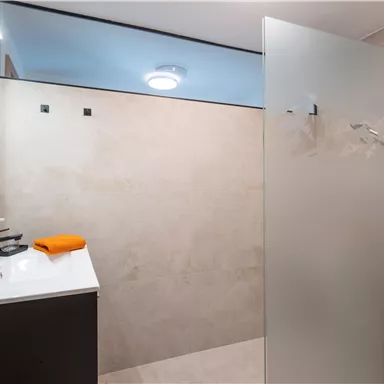 A modern laundry room with a shower and a washing machine. The walls are brightly tiled, and there are orange towels on the countertop.