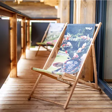 A cozy terrace with wooden lounge chairs. The chairs are decorated with colorful motifs and invite you to relax.