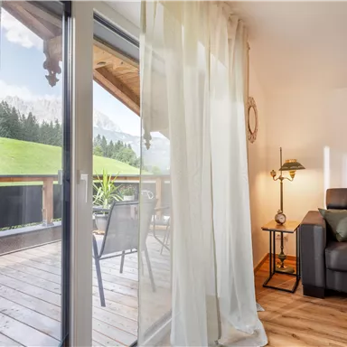 A cozy living space with a gray sofa and a floor lamp. Through the large windows, there is a view of a green landscape.