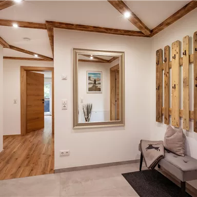 A modern hallway with wooden details and a large mirror. Wooden strips hang on the wall, and a side chair provides additional comfort.