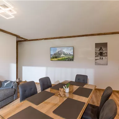 A modern dining area with a large wooden table and black chairs.
On the wall hang pictures of a mountain landscape and a person cycling.